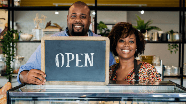 black man and black woman holding an open sign in their business